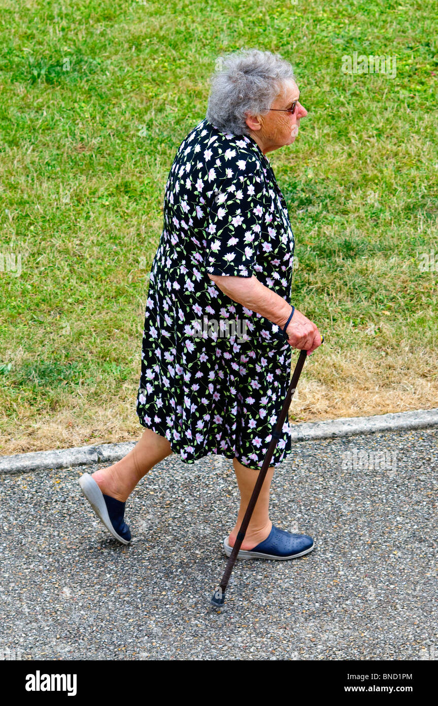 Femme âgée avec bâton de marche marche le long trottoir - France. Banque D'Images