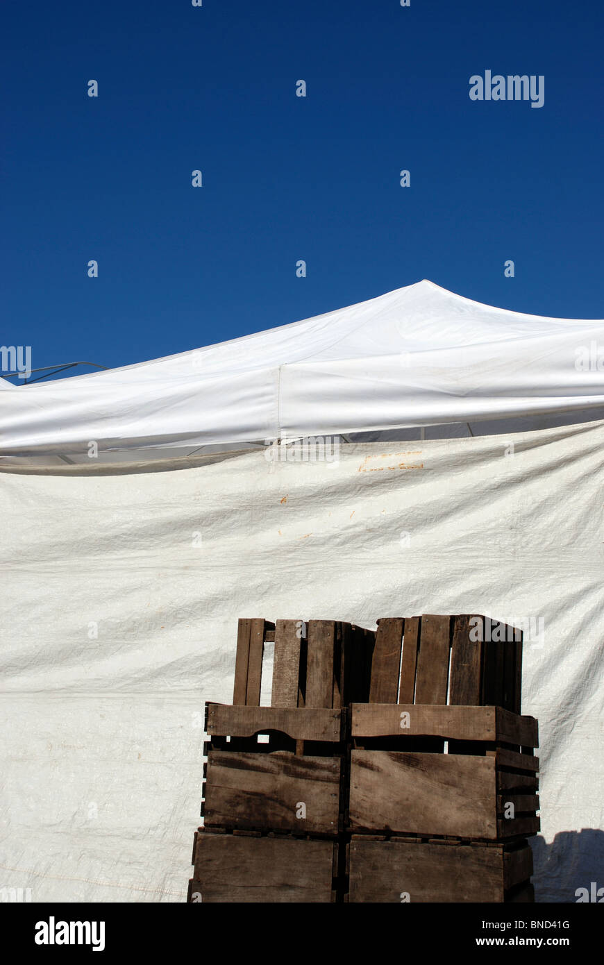 Caisses en bois contre une tente blanche à un marché de producteurs sous un ciel bleu clair. Banque D'Images
