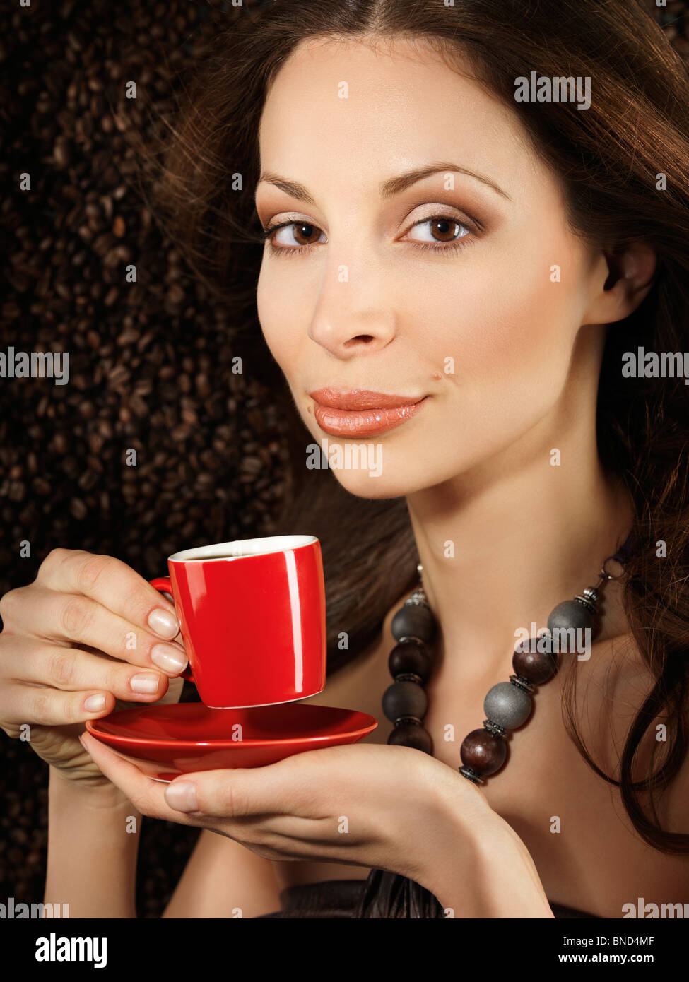 Belle Jeune femme tenant une tasse de café espresso rouge avec des haricots de café derrière elle en arrière-plan Banque D'Images
