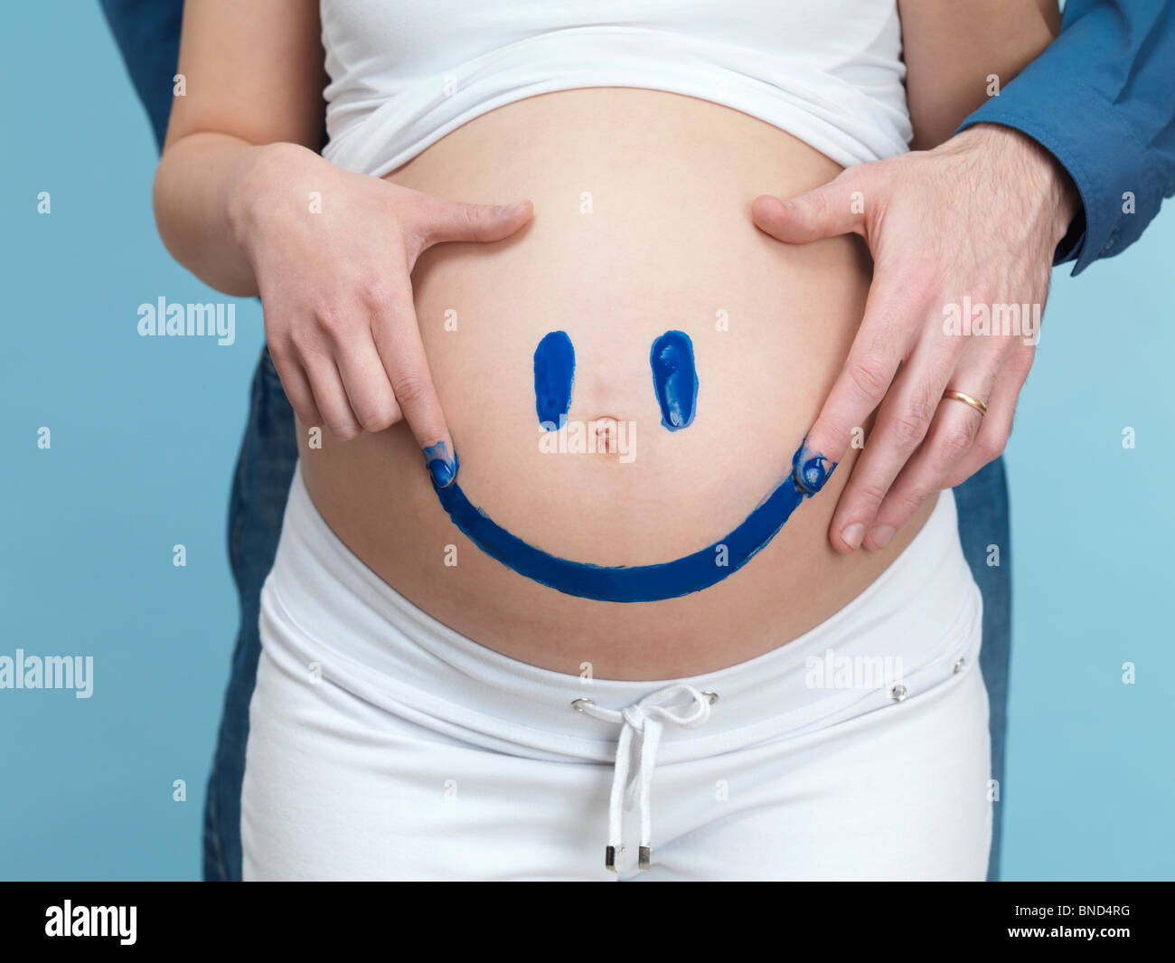 Jeune femme enceinte et son mari à peindre un visage heureux sur son ventre. Banque D'Images