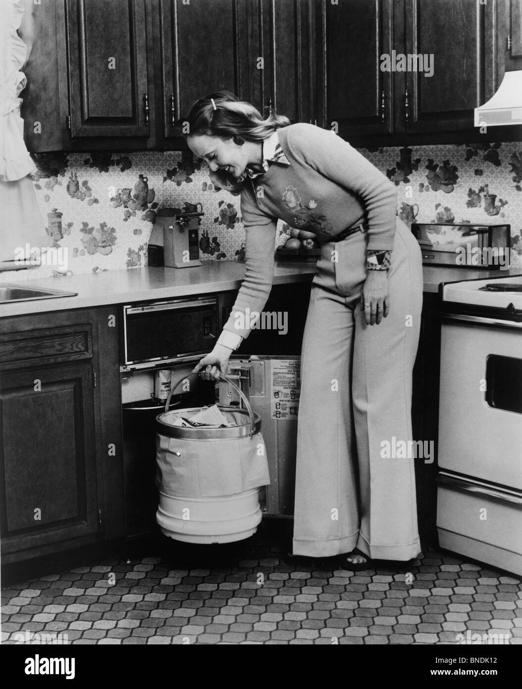 Jeune femme debout dans la cuisine avec une poubelle Banque D'Images