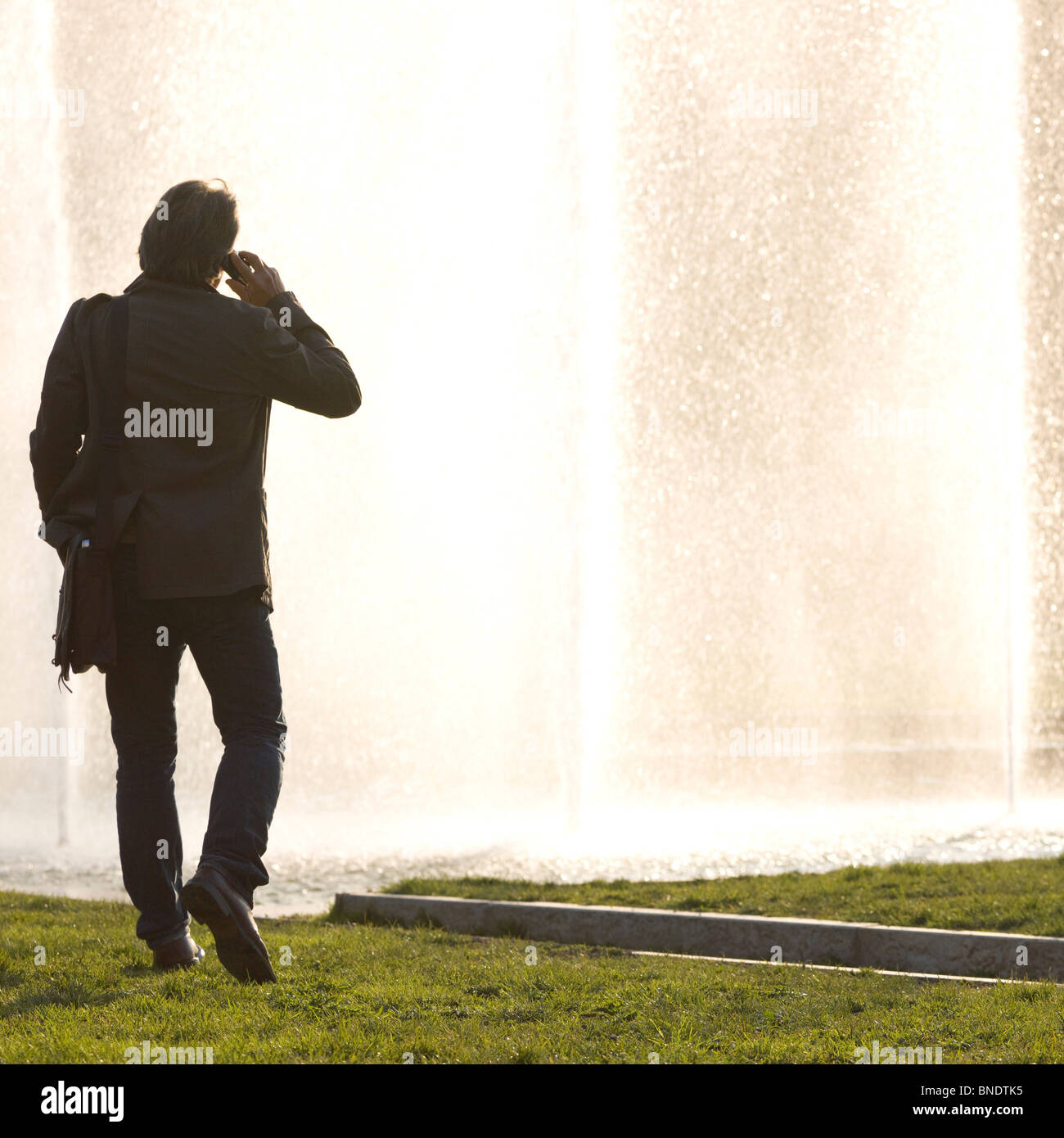 Man talking on a mobile phone en face d'une fontaine Banque D'Images