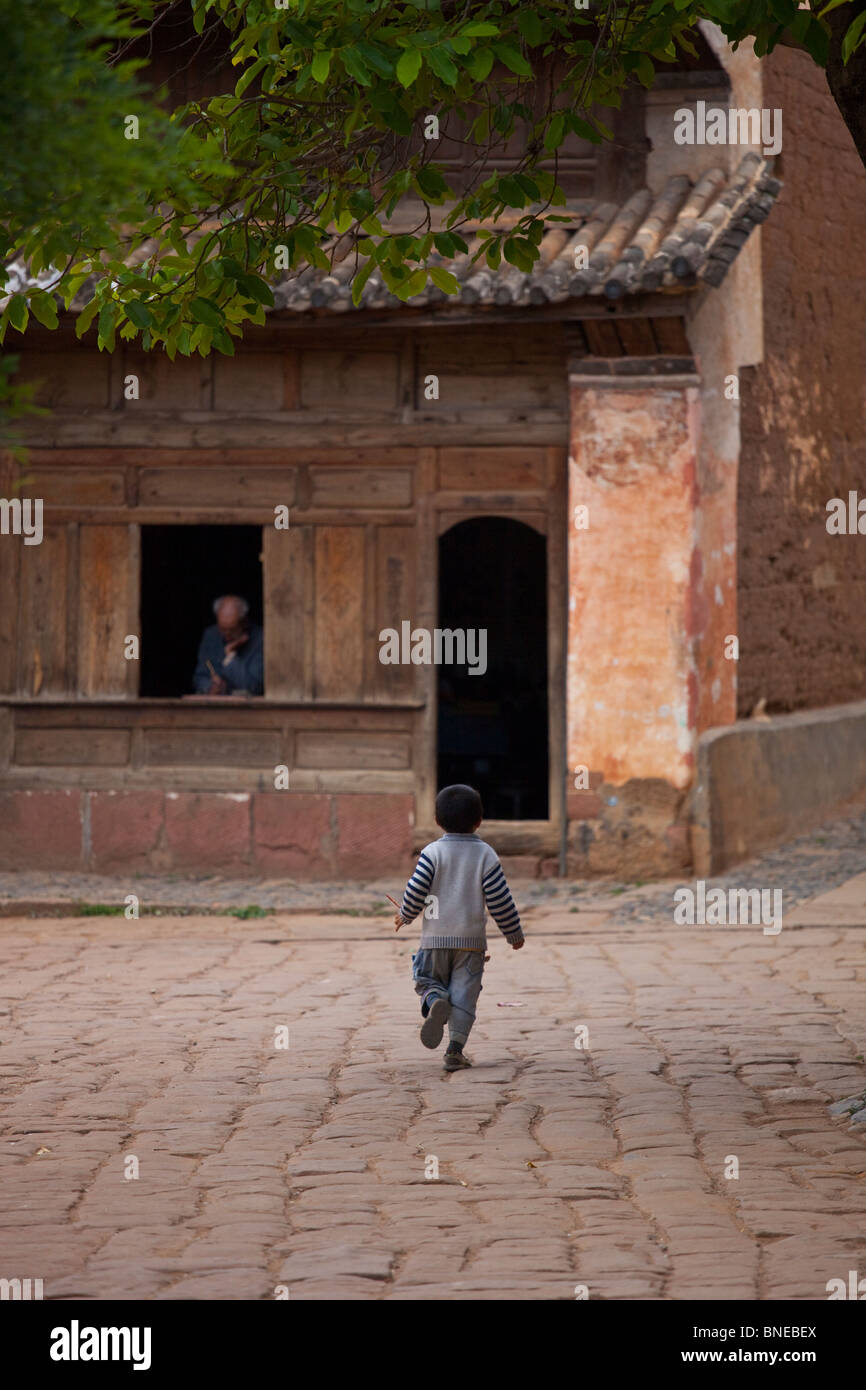 Boy running sur la place principale de Shaxi, Village de la province de Yunnan, Chine Banque D'Images