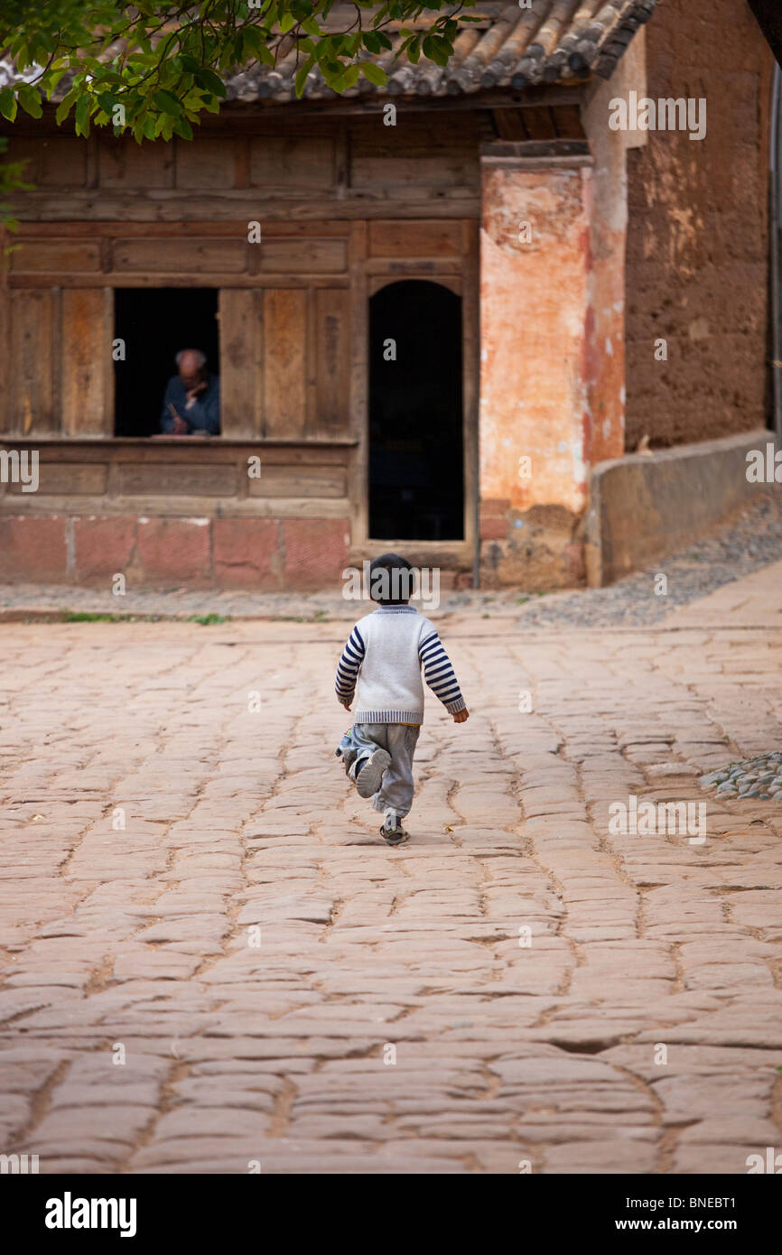 Boy running sur la place principale de Shaxi, Village de la province de Yunnan, Chine Banque D'Images