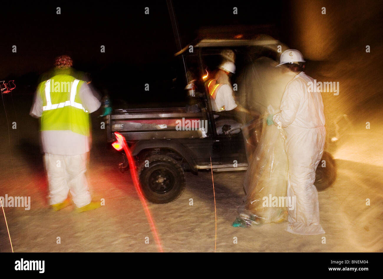 L'exposition dans le temps de 3 travailleurs de l'assainissement le nettoyage des déversements de pétrole au mess nuit sur un plage du Mississippi. Juillet 2010. Banque D'Images