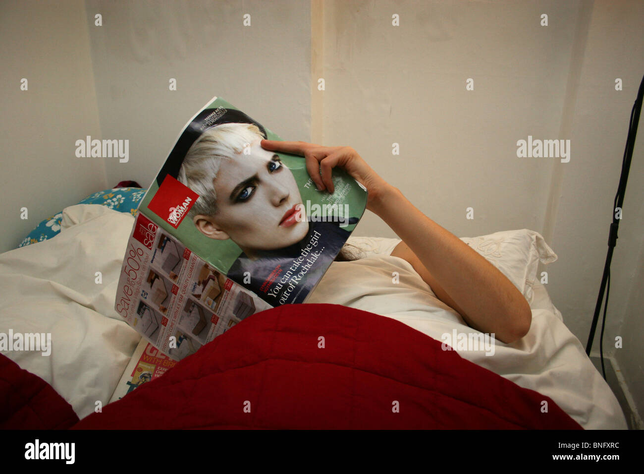 Femme au lit la lecture d'une copie de l'Observateur d' Agyness Deyn Femme sur le capot avant, au Royaume-Uni. Banque D'Images
