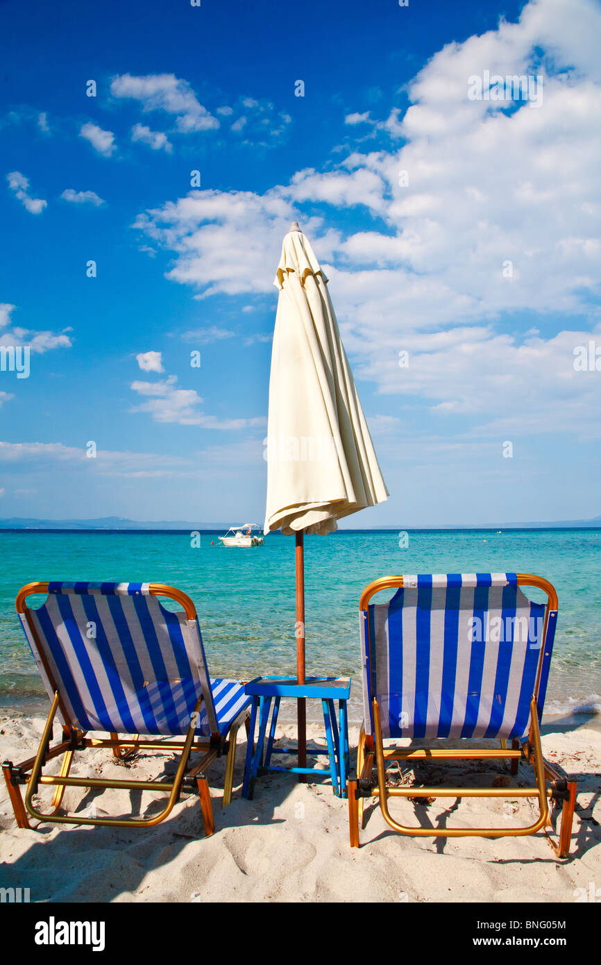Une plage de sable couverts en Grèce montre deux rayures bleu, vide de chaises longues dans l'attente de clients. Il y a un pare-soleil entre eux. Banque D'Images