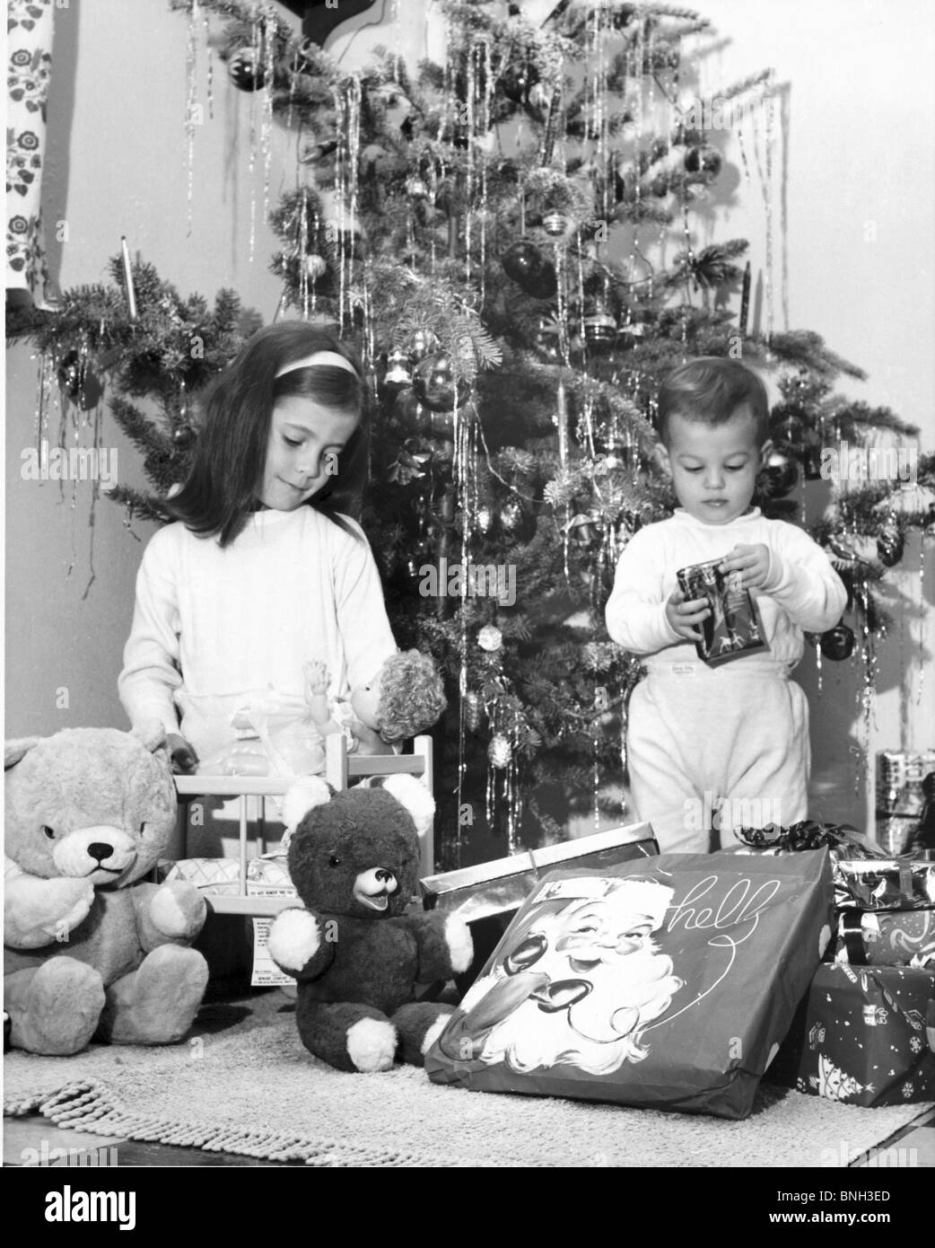Fille jouant avec une poupée et son frère l'ouverture d'un cadeau de Noël à ses côtés Banque D'Images