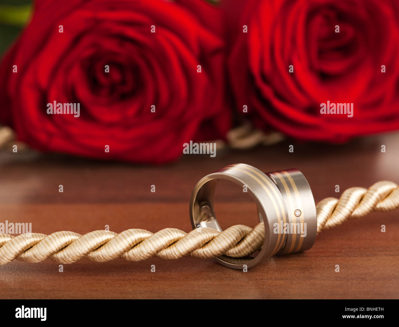Anneaux de mariage de titane et or sur cordon, roses rouges en arrière-plan Banque D'Images