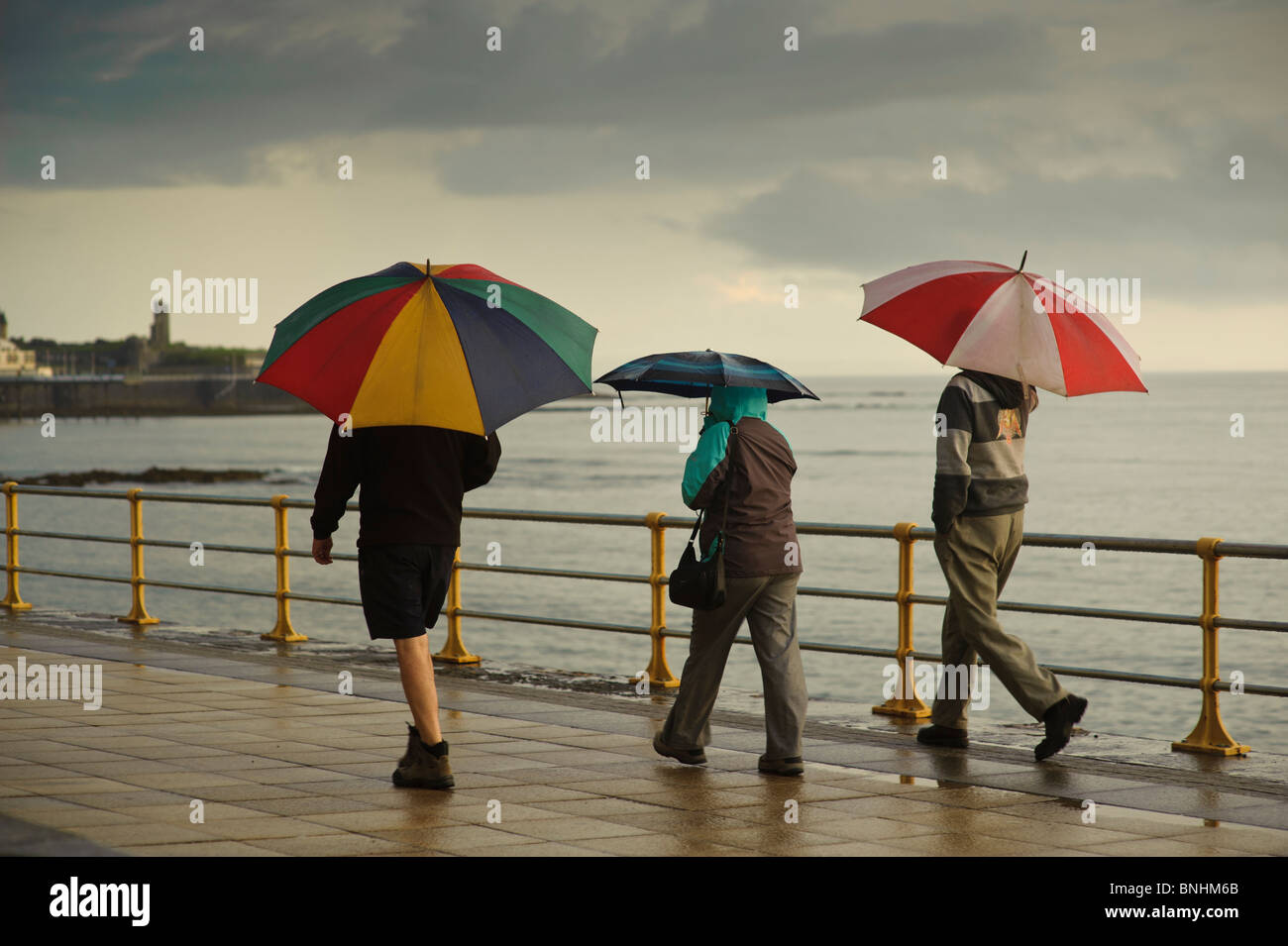 Trois personnes s'abritant sous des parasols sur une soirée d'été humide, Aberystwyth Wales UK Banque D'Images