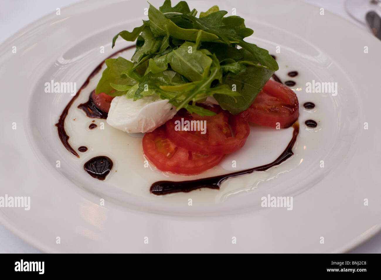 Tomates mûres fraîches servi avec mozzarella di buffala, roquette, sont habillés avec une réduction de balsamique et d'huile d'olive. Banque D'Images