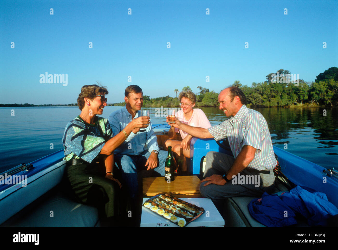 Les touristes ayant des cocktails au coucher pendant une excursion en bateau sur la rivière Zambèze entre la Zambie et le Zimbabwe Banque D'Images