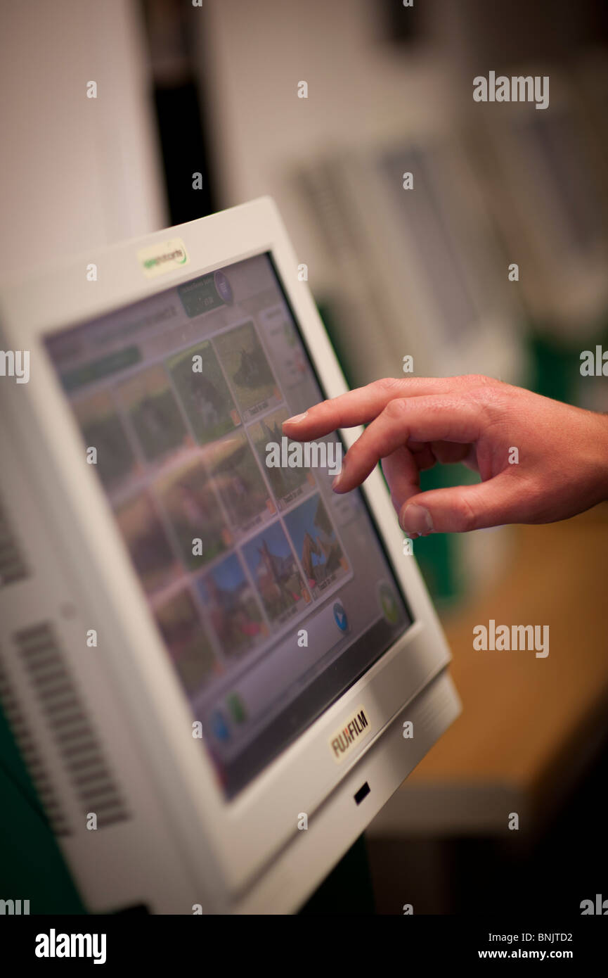 Client en utilisant un écran tactile terminal d'ordinateur de choisir et de commander des tirages à un laboratoire de développement photo de rue, UK Banque D'Images