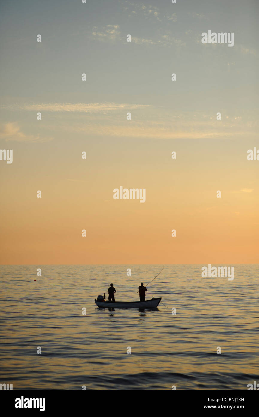 Deux pêcheurs au coucher du soleil dans un petit bateau sur la baie de Cardigan, West Wales UK Banque D'Images