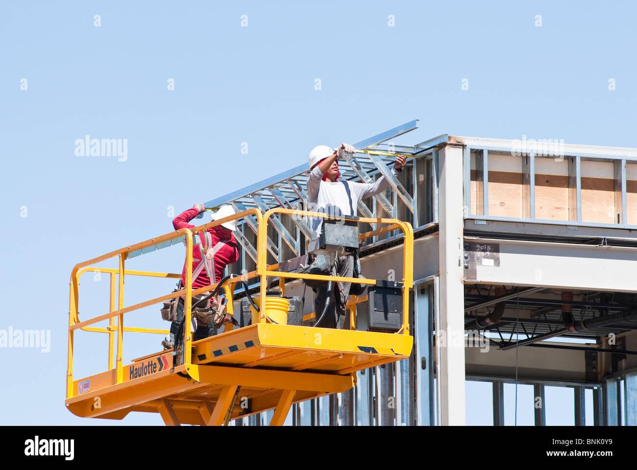 Les travailleurs de la construction sur une plate-forme élévatrice à ciseaux sont l'assemblage de membrures en acier sur un nouveau bâtiment commercial. Banque D'Images
