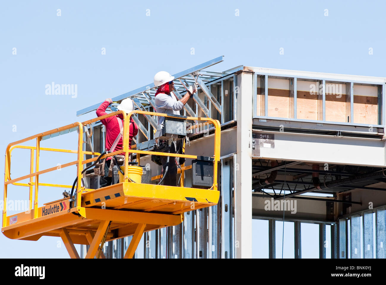 Les travailleurs de la construction sur une plate-forme élévatrice à ciseaux sont l'assemblage de membrures en acier sur un nouveau bâtiment commercial. Banque D'Images