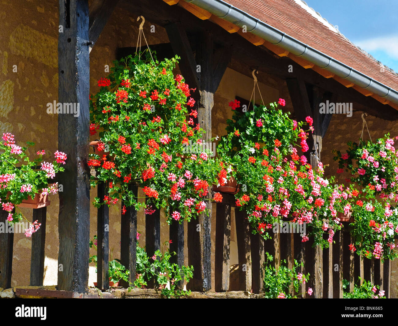 Paniers suspendus et des jardinières sur le balcon en bois de la maison en pierre - France. Banque D'Images