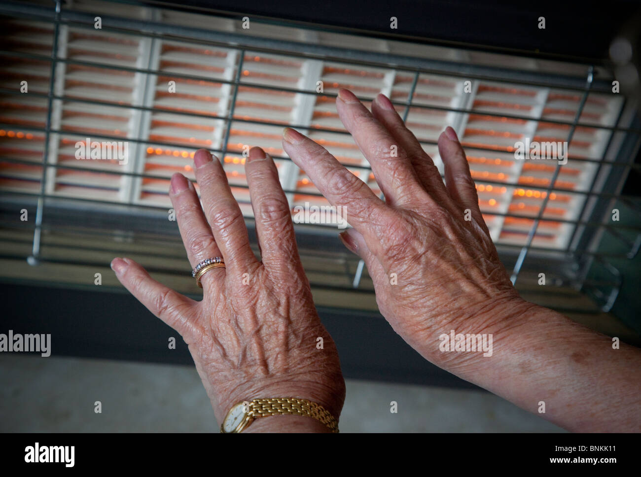Les mains d'un pensionné de la vieillesse en face d'un feu de gaz pour garder au chaud pendant les mois d'hiver Banque D'Images