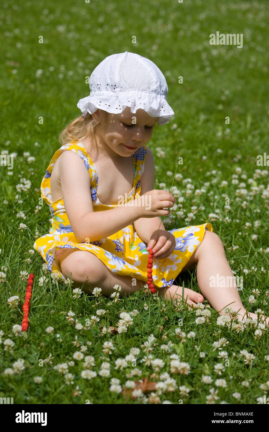 Trois ans, assis sur l'herbe, des fraises sur une paille de l'herbe Banque D'Images