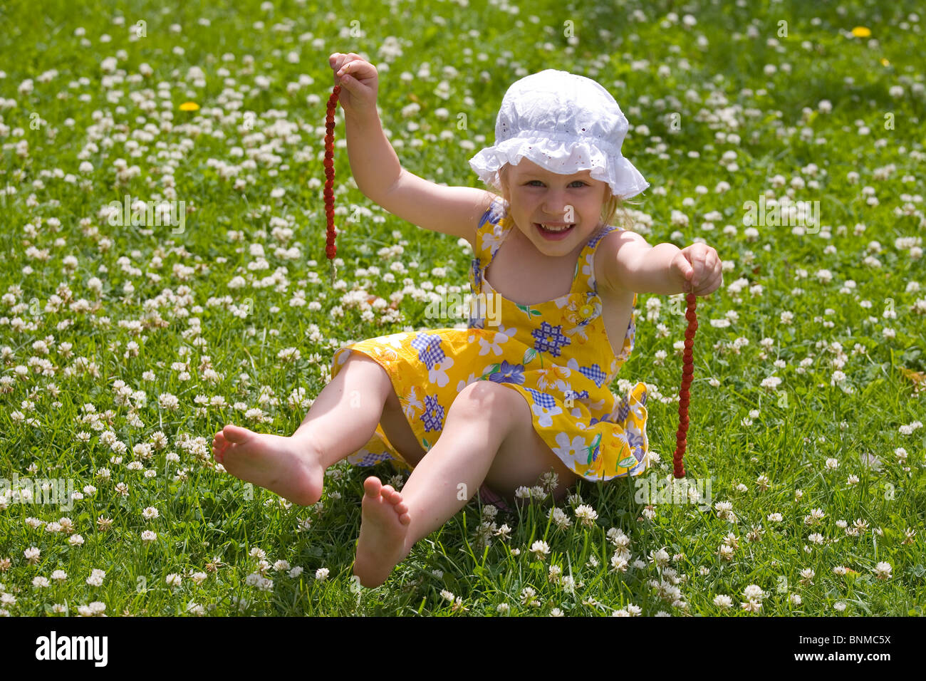 Trois ans, assis sur l'herbe, les fraises sur un Grasstraw Banque D'Images