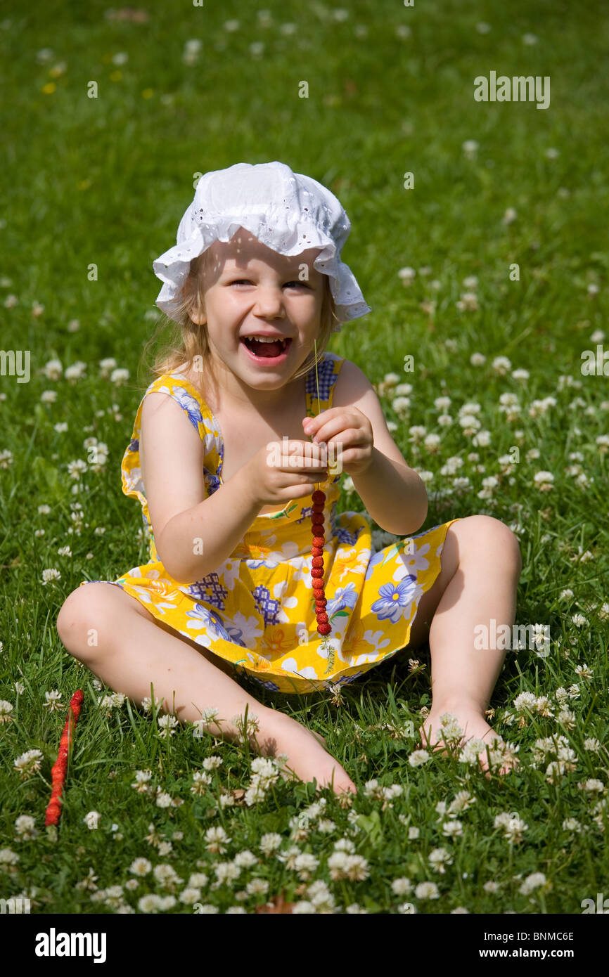 Trois ans, assis sur l'herbe, les fraises sur un Grasstraw Banque D'Images