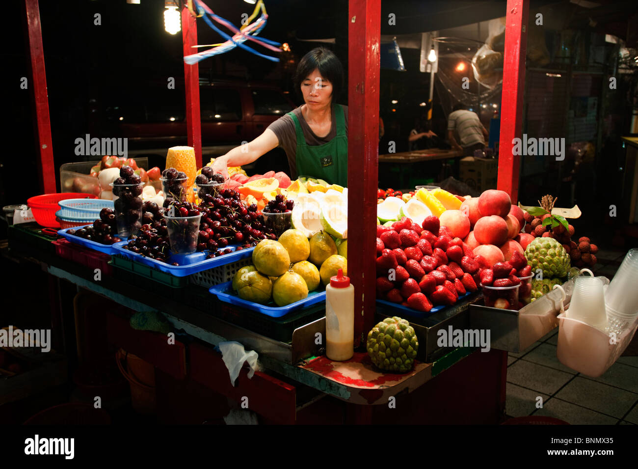 Un stand vendant une grande variété de fruits et baies affiche ses marchandises sous les lumières vives dans le marché de nuit de Taipei. Banque D'Images