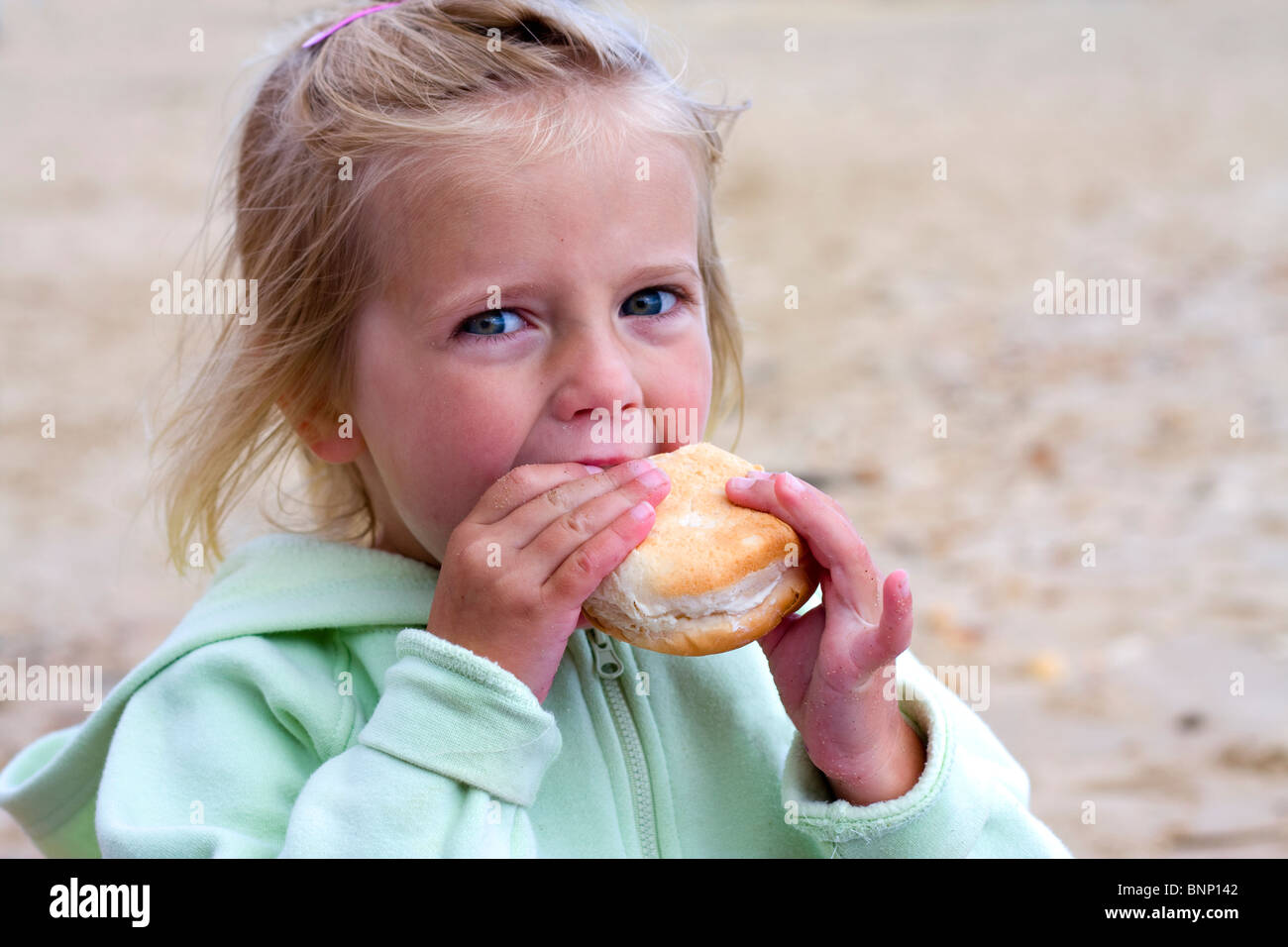 Jeune fille en train de manger un sandwich sur la plage Banque D'Images