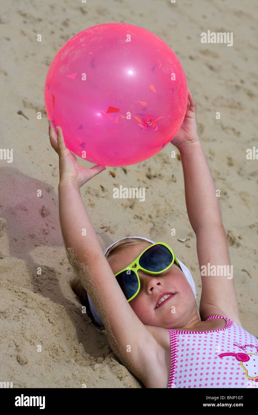 Jeune fille portant sur le sable tenant une balle rose Banque D'Images