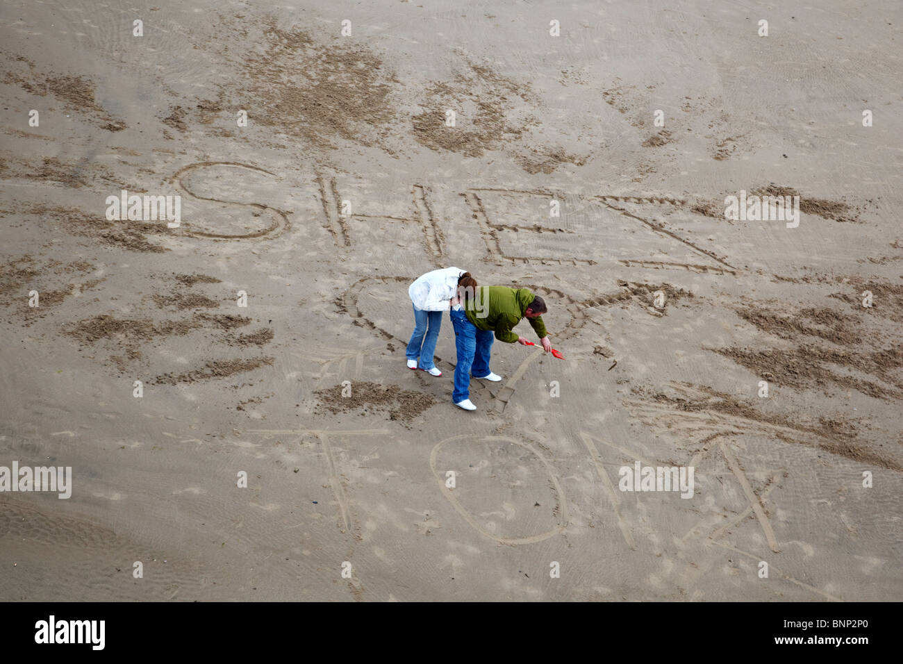 Un couple dans l'amour dessine un coeur sur la plage de Blackpool, Angleterre. Banque D'Images