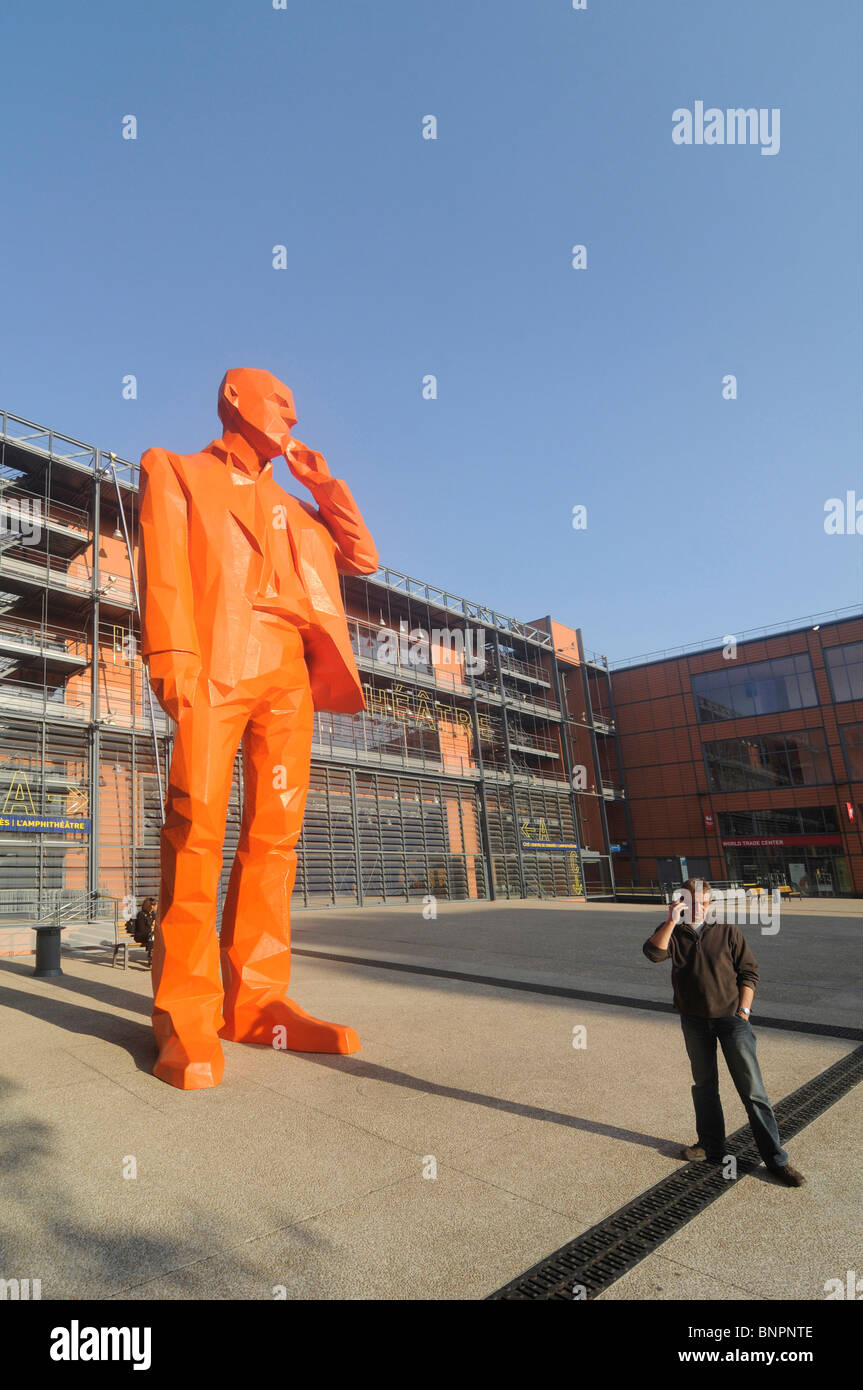 Un homme à l'aide de son téléphone portable à proximité d'une statue géante montrant un homme avec un téléphone mobile dans la cité internationale à Lyon, France. Banque D'Images