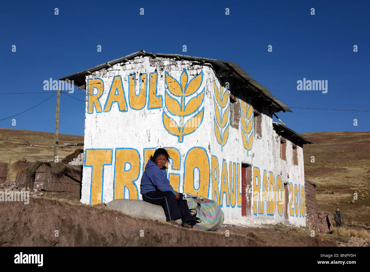 Fille assise sur le rocher à l'extérieur de la maison peinte avec de la propagande pour le candidat du Parti du blé pour les élections locales, près de Yanaoca, région de Cusco, Pérou Banque D'Images