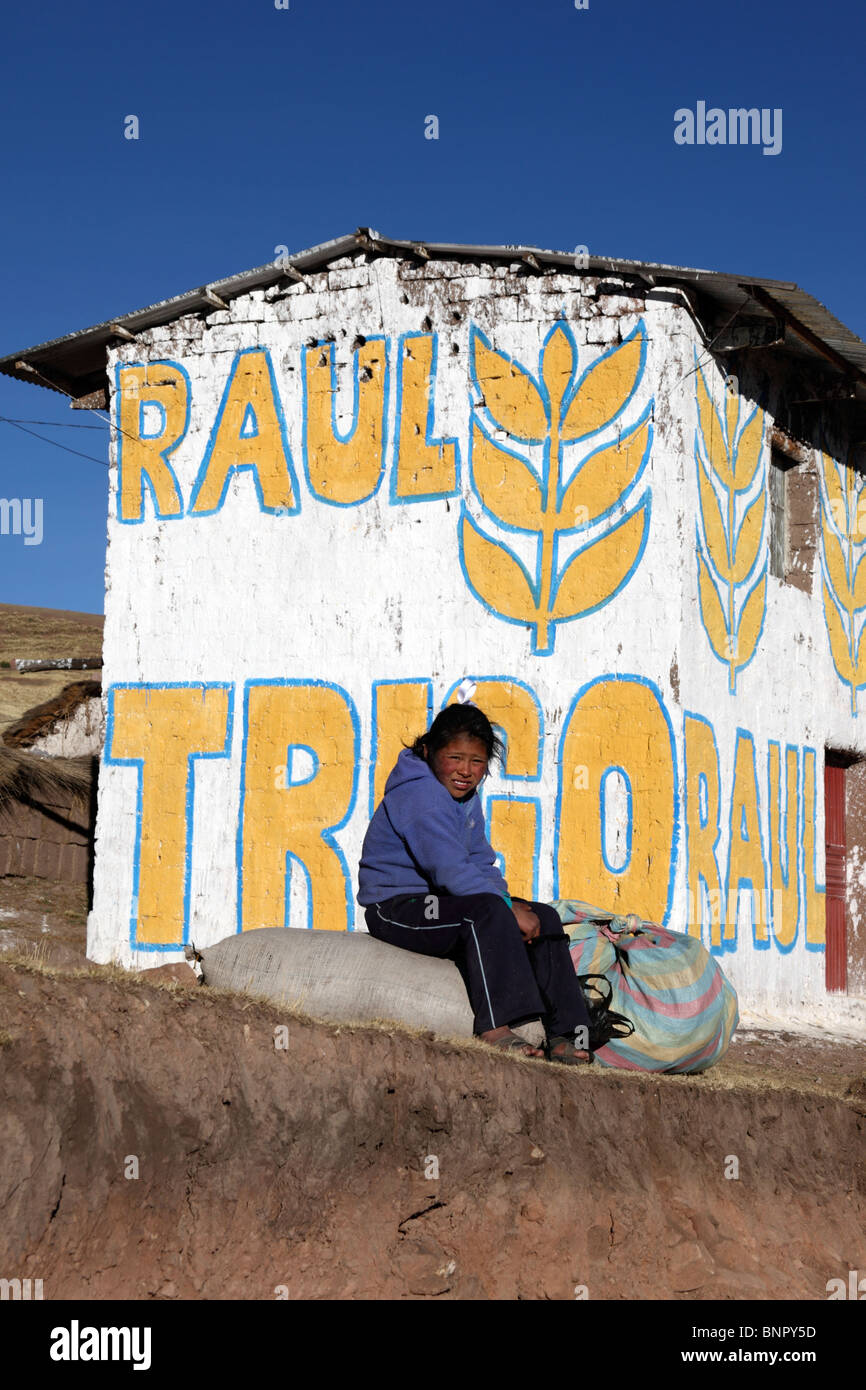 Fille assise sur le rocher à l'extérieur de la maison peinte avec de la propagande pour le candidat du Parti du blé pour les élections locales, près de Yanaoca, région de Cusco, Pérou Banque D'Images