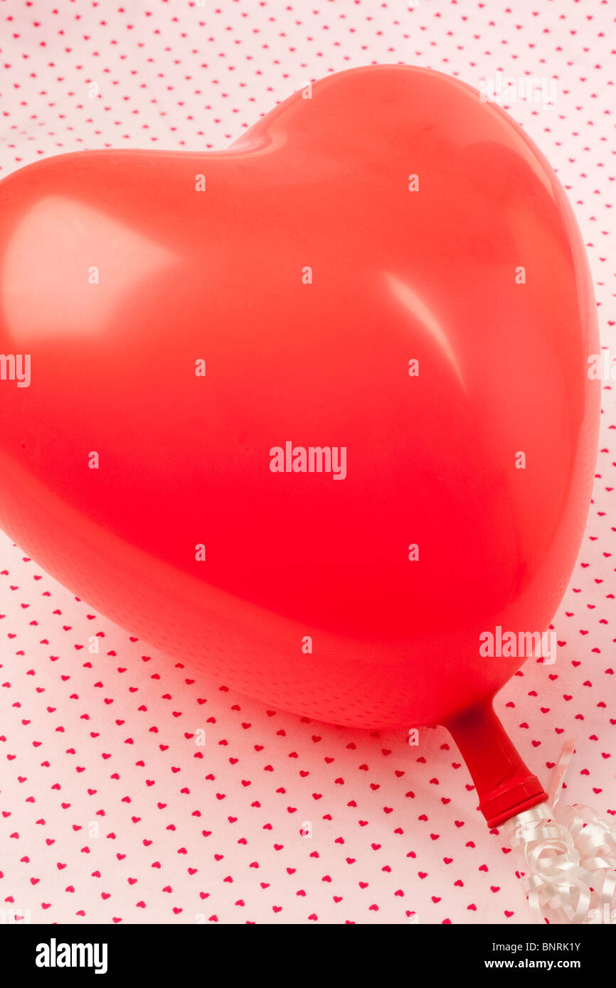 Un ballon en forme de coeur rouge sur un fond de lumière de petits coeurs roses Banque D'Images