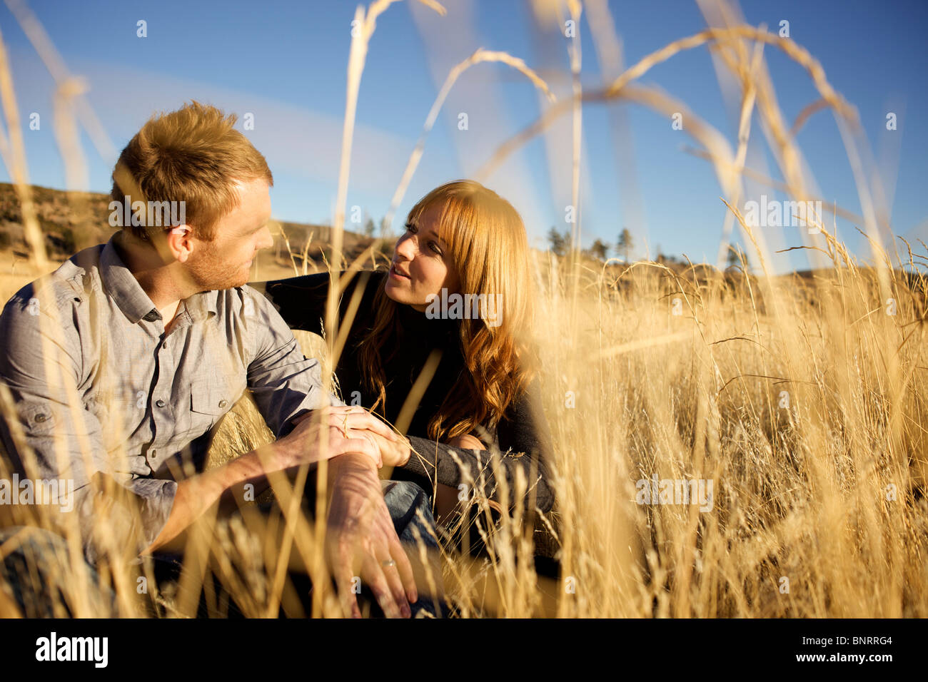 Couple assis sur le sol d'un champ ouvert se regarder et sourire. Banque D'Images Couple assis sur le sol d'un champ ouvert se regarder et sourire. Banque D'Images