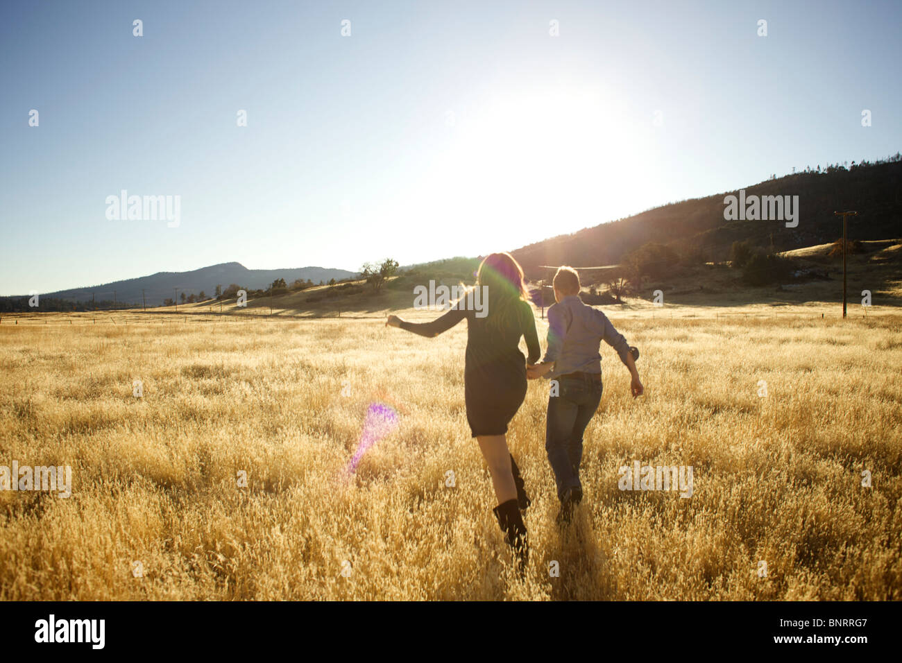Couple tenir la main et courir ensemble dans un champ ouvert. Banque D'Images Couple tenir la main et courir ensemble dans un champ ouvert. Banque D'Images