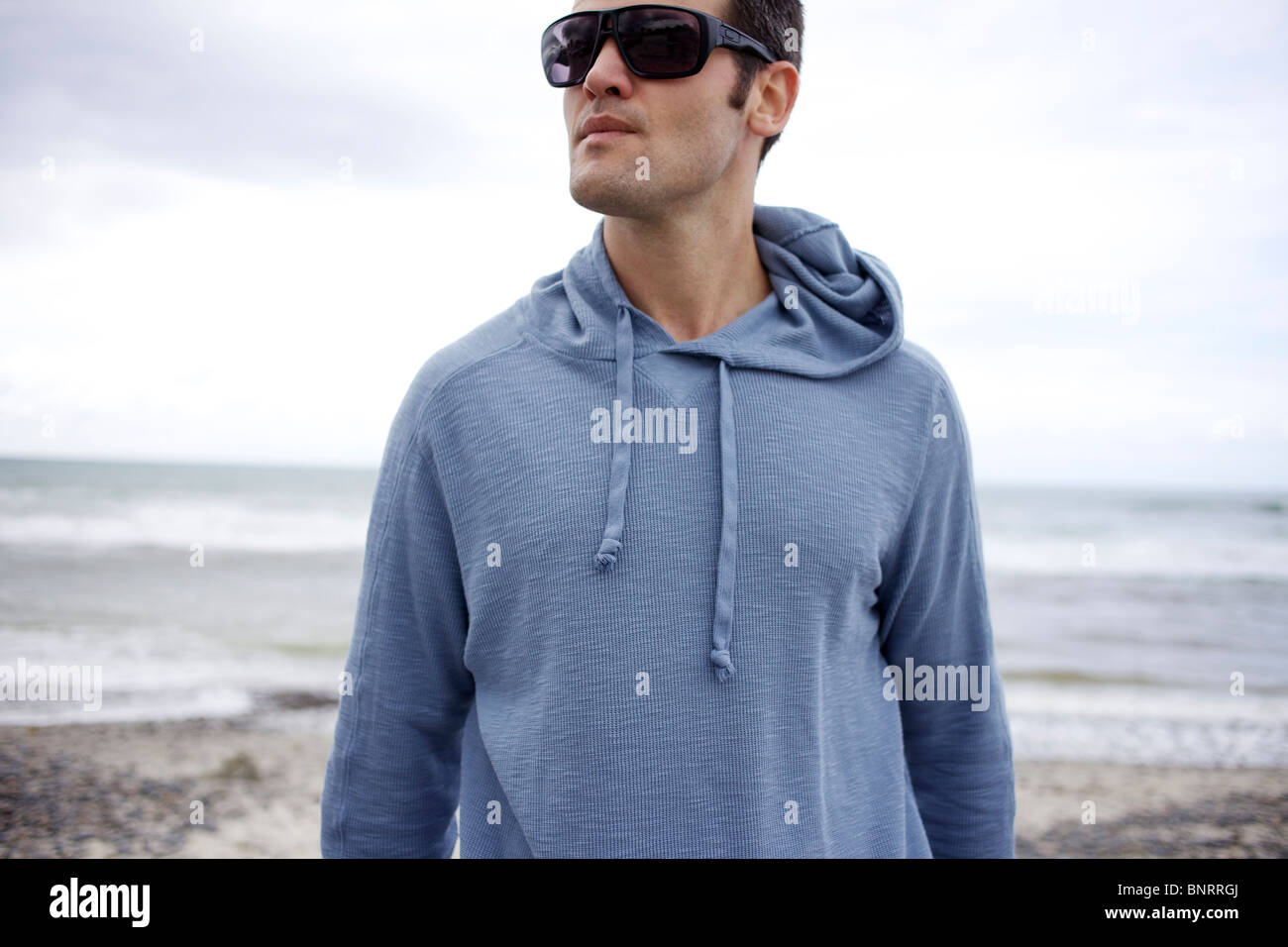 Homme portant des lunettes de soleil et un grand sweat à la plage. Banque D'Images Homme portant des lunettes de soleil et un grand sweat à la plage. Banque D'Images