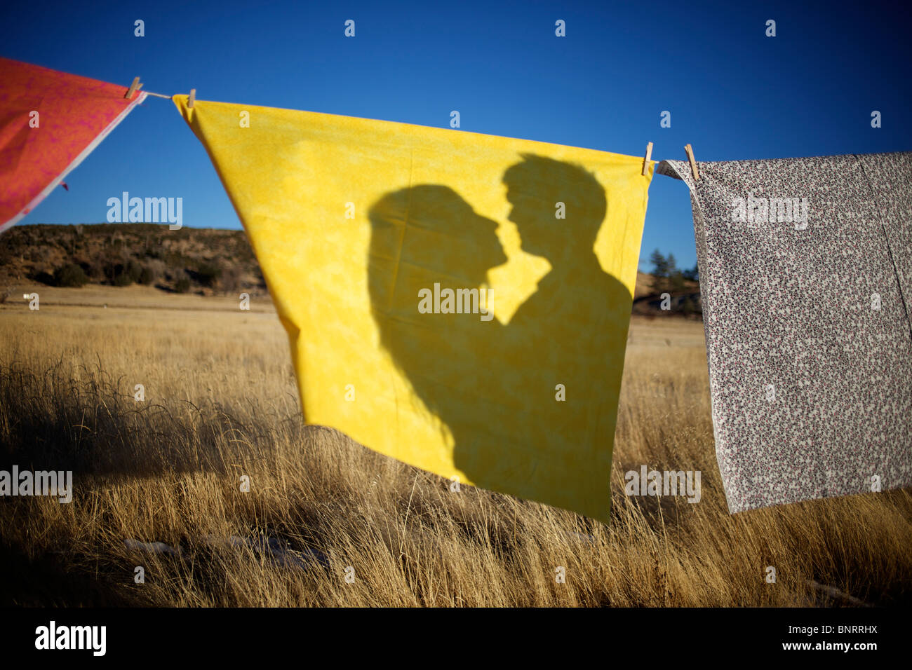 Un couple's Shadow sur un tissu jaune accroché sur une corde à linge dans un champ ouvert. Banque D'Images Un couple's Shadow sur un tissu jaune accroché sur une corde à linge dans un champ ouvert. Banque D'Images