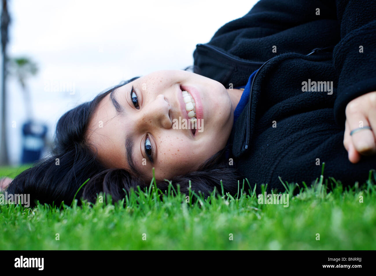 Une jeune fille s'étend dans l'herbe, regarde la caméra et sourit au parc. Banque D'Images Une jeune fille s'étend dans l'herbe, regarde la caméra et sourit au parc. Banque D'Images