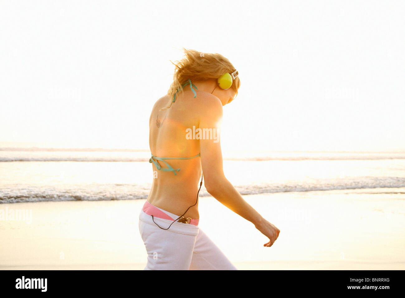 Jeune femme portant un casque s'en va à la plage pendant le coucher du soleil. Banque D'Images Jeune femme portant un casque s'en va à la plage pendant le coucher du soleil. Banque D'Images