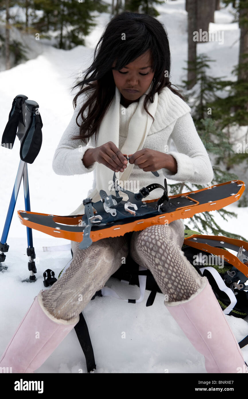 Portrait of a young African American Woman assis sur son sac à dos dans la neige travail sur sa raquette. Banque D'Images