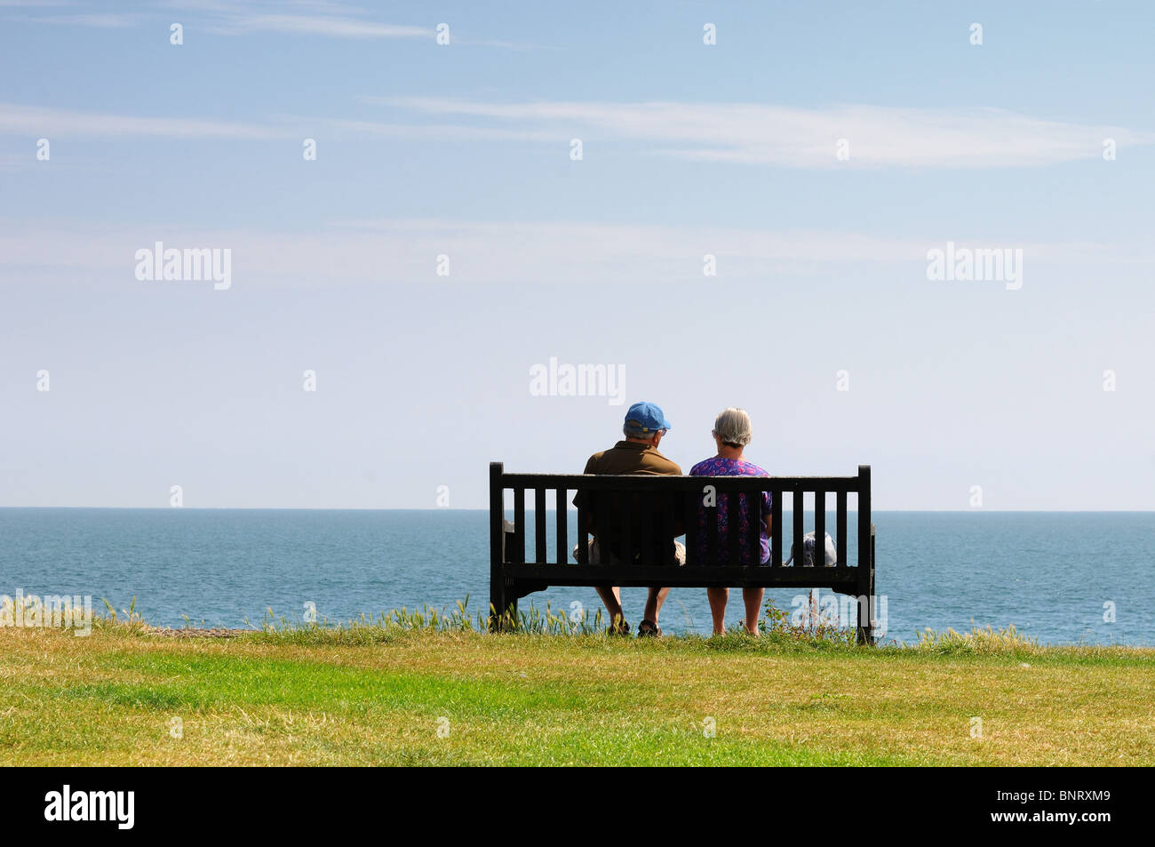 Vue arrière du couple de personnes âgées assis sur banc de falaise face à la mer Banque D'Images
