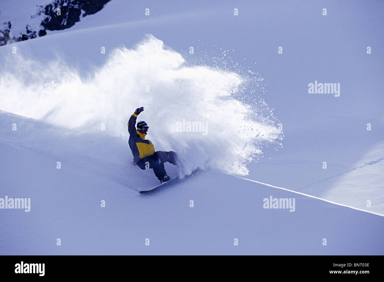 Snowboarder dans yellow jacket coups de pied un grand panache de poudreuse. Banque D'Images