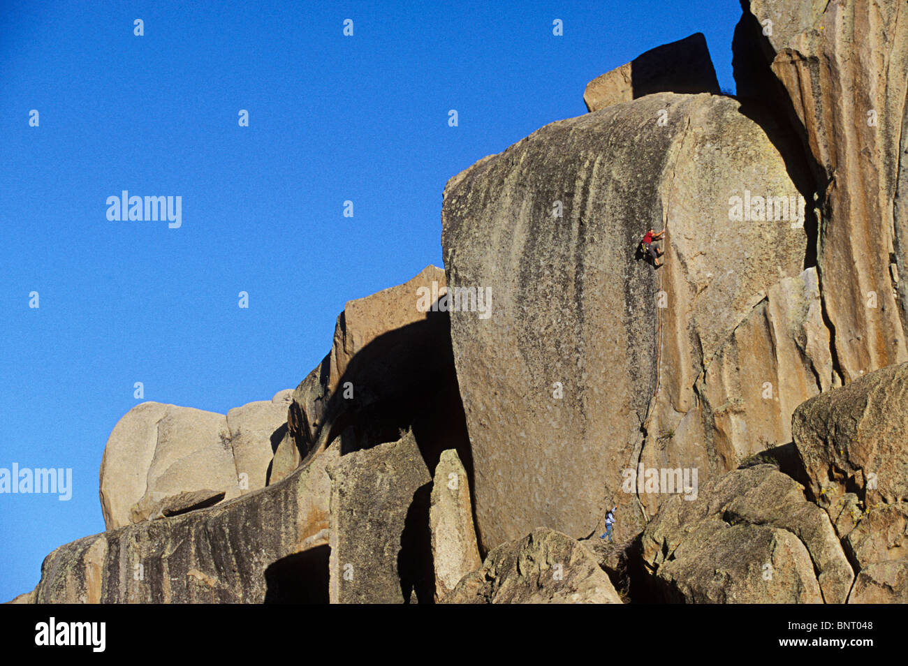 Un alpiniste et son assureur semblent petits contre la grande roche. Banque D'Images