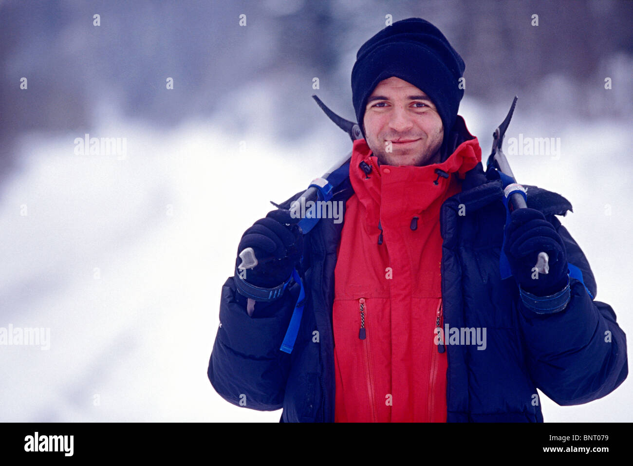 L'homme se dresse dans la neige holding piolets sur ses épaules. Banque D'Images