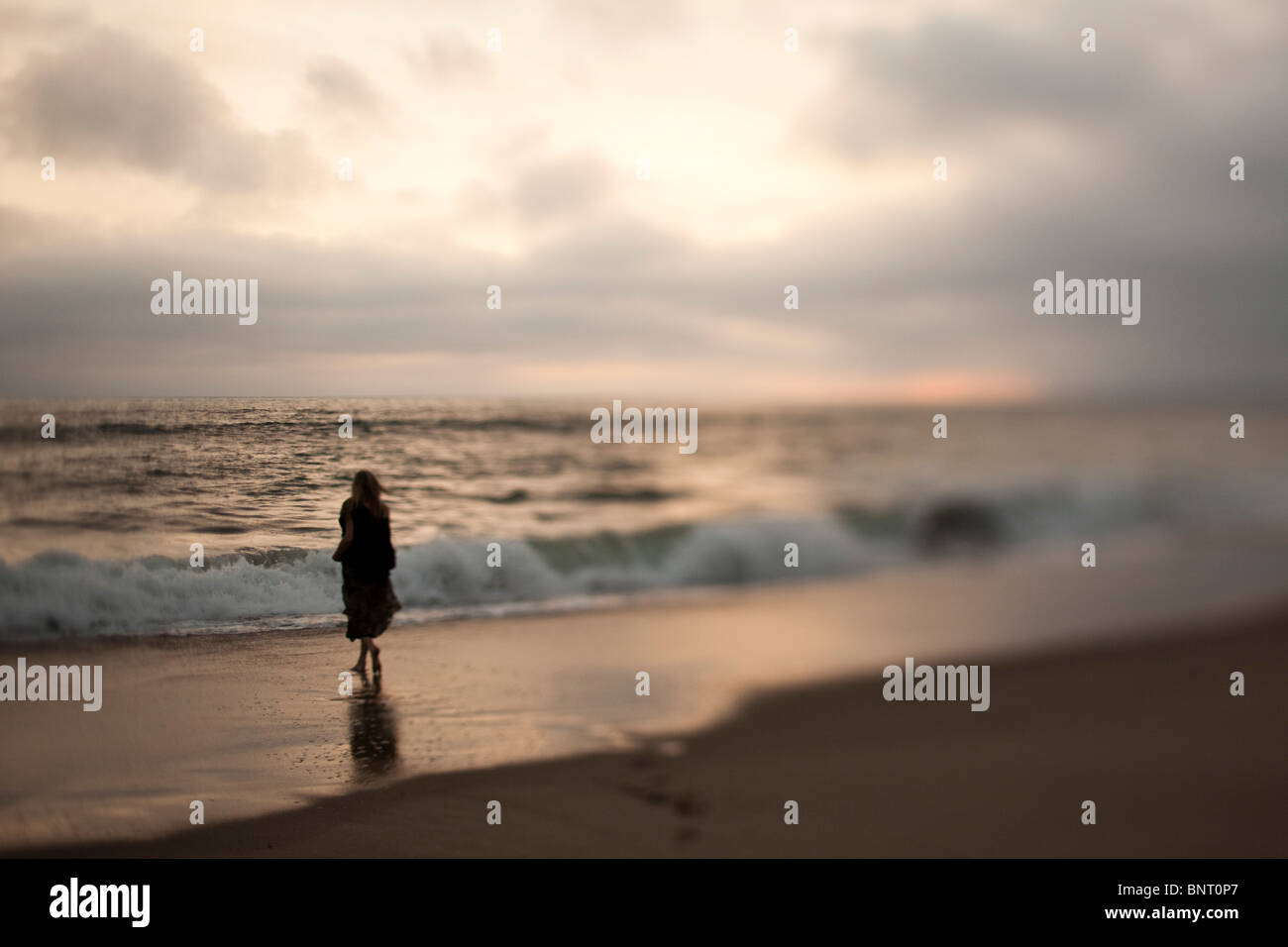Une femme marche sur une plage au coucher du soleil en Californie. Banque D'Images