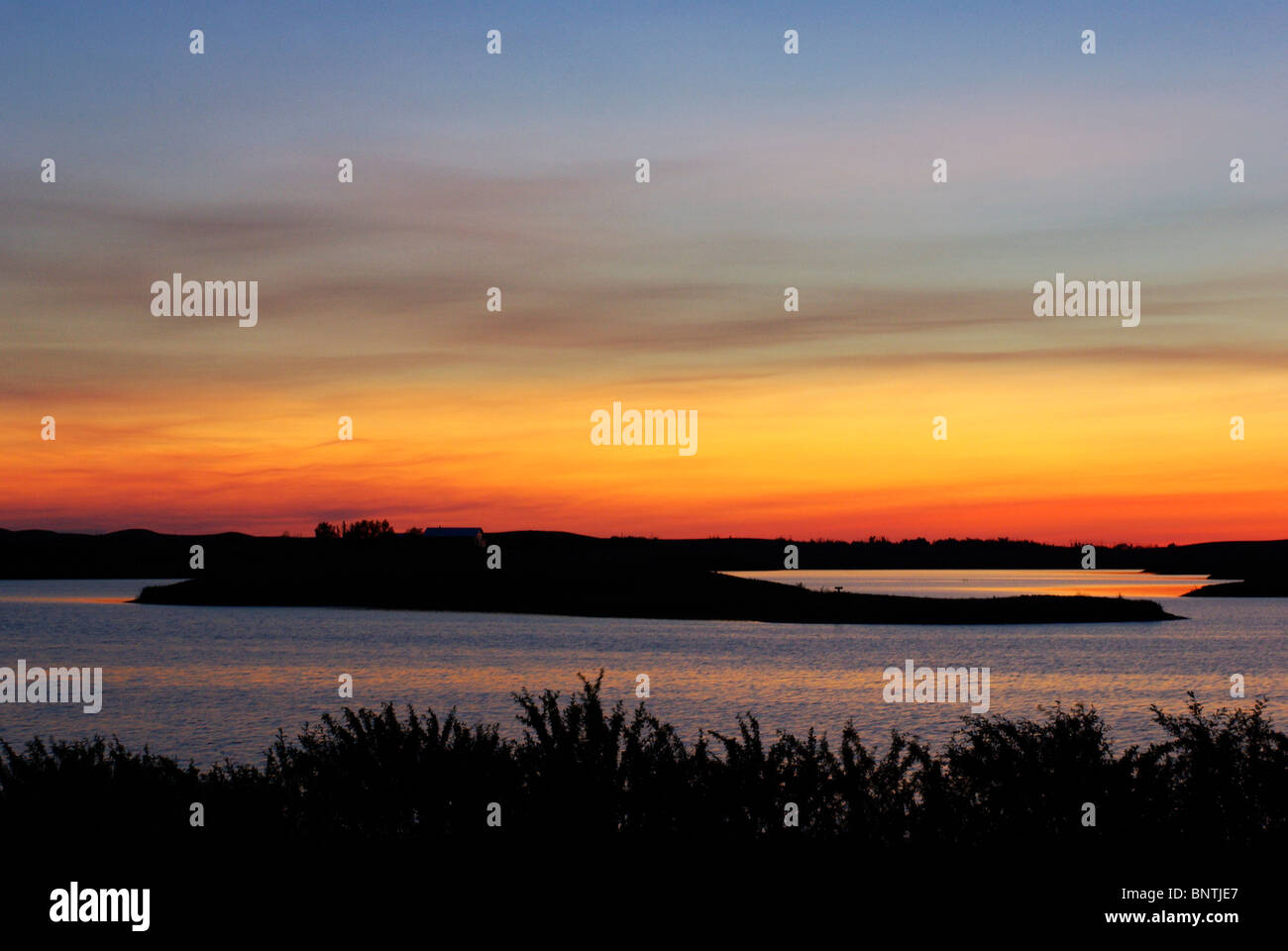 Coucher du soleil capturé sur un lac des Prairies en Alberta, Canada. Il y a le feuillage et une petite île silhoutte of mountain range at sunset. Banque D'Images