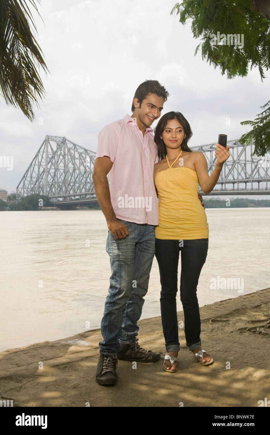 Couple de prendre une photo d'eux-mêmes avec un pont en arrière-plan, Howrah Bridge, rivière Hooghly, Kolkata, West Bengal, India Banque D'Images