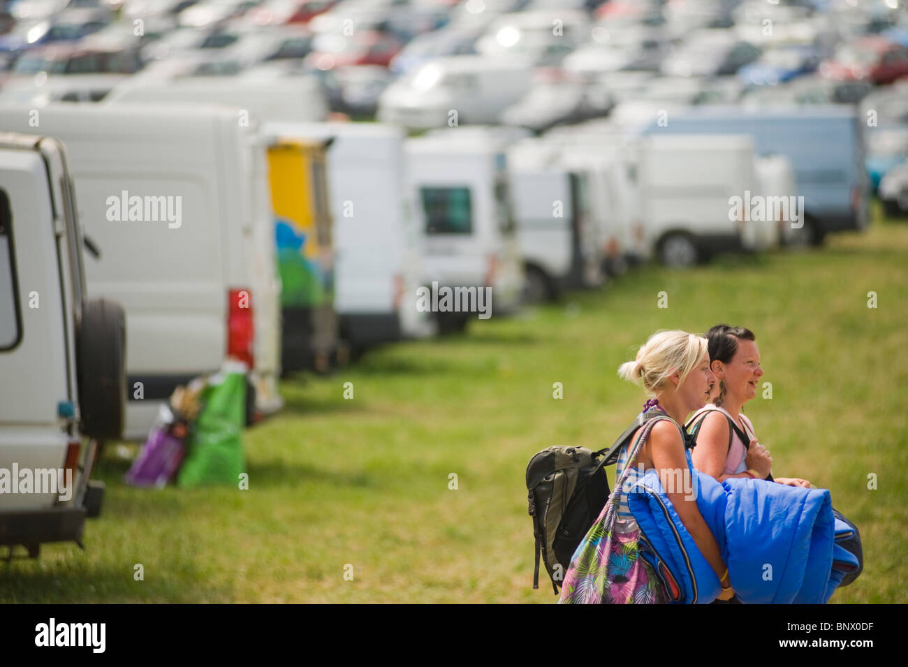 Les gens quittant le Glastonbury Festival à la fin du festival avec des voitures en stationnement et cars à l'arrière-plan. Banque D'Images