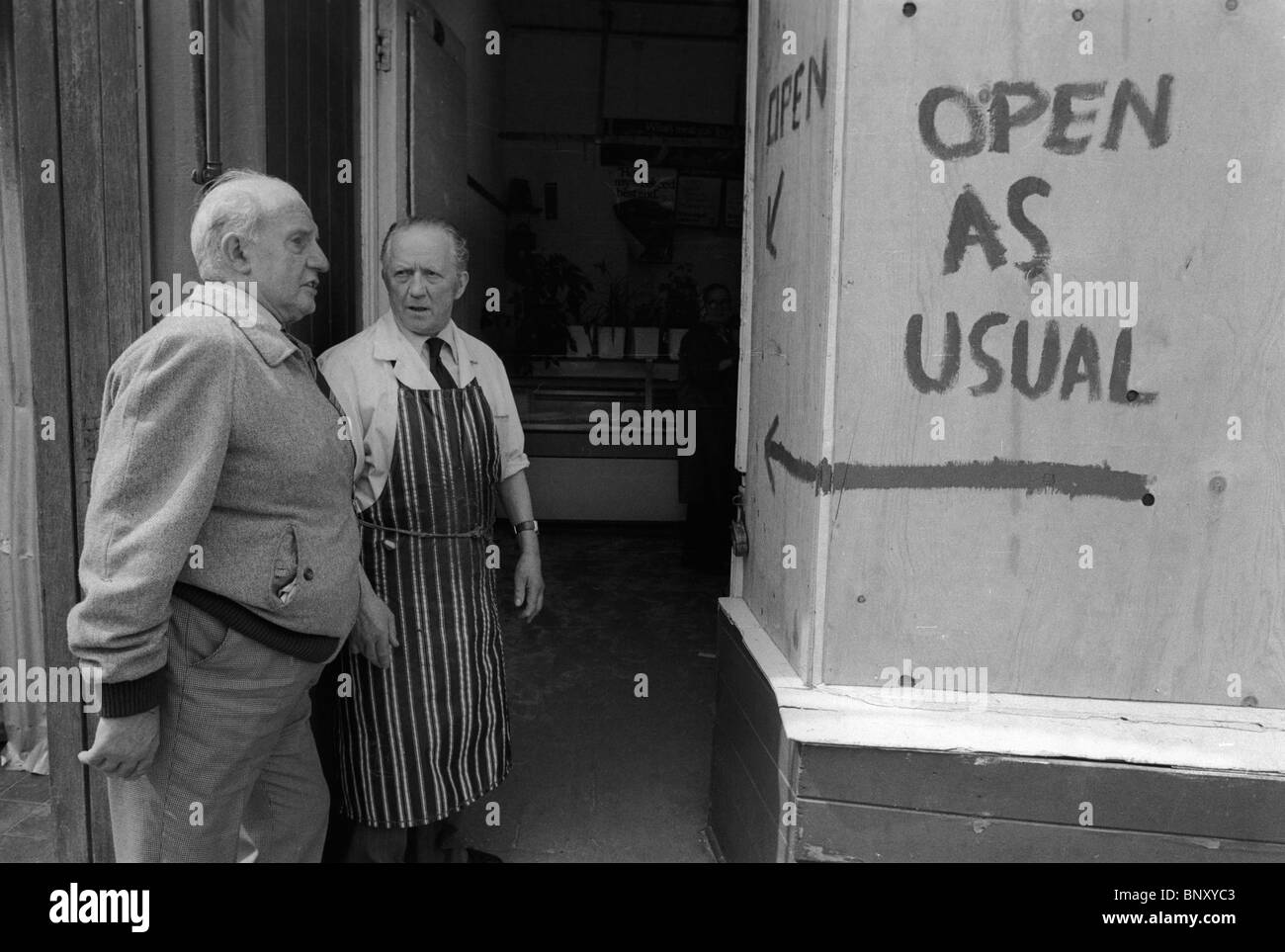 Toxteth Riot 1980s Royaume-Uni. Un boucher dans son tablier de boucherie se tient devant son magasin pour parler à une personne locale. La boucherie a été pillée – la veille pendant les émeutes, et est maintenant embarquée, mais ouverte comme d’habitude malgré tout. Liverpool 8, Lancashire, Angleterre juillet 1981. HOMER SYKES Banque D'Images