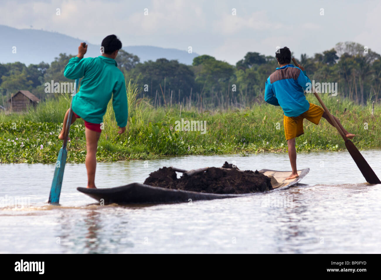 Deux hommes ethnie Intha unijambistes ramer sur un bateau avec de la terre sur le lac Inle, Myanmar Banque D'Images